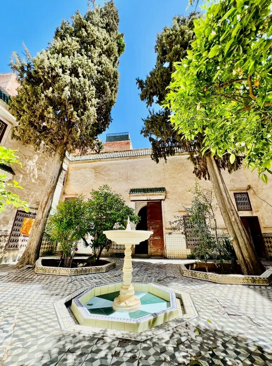 Open courtyard with trees, greenery, and a central fountain in Kaat Ben Nahid.