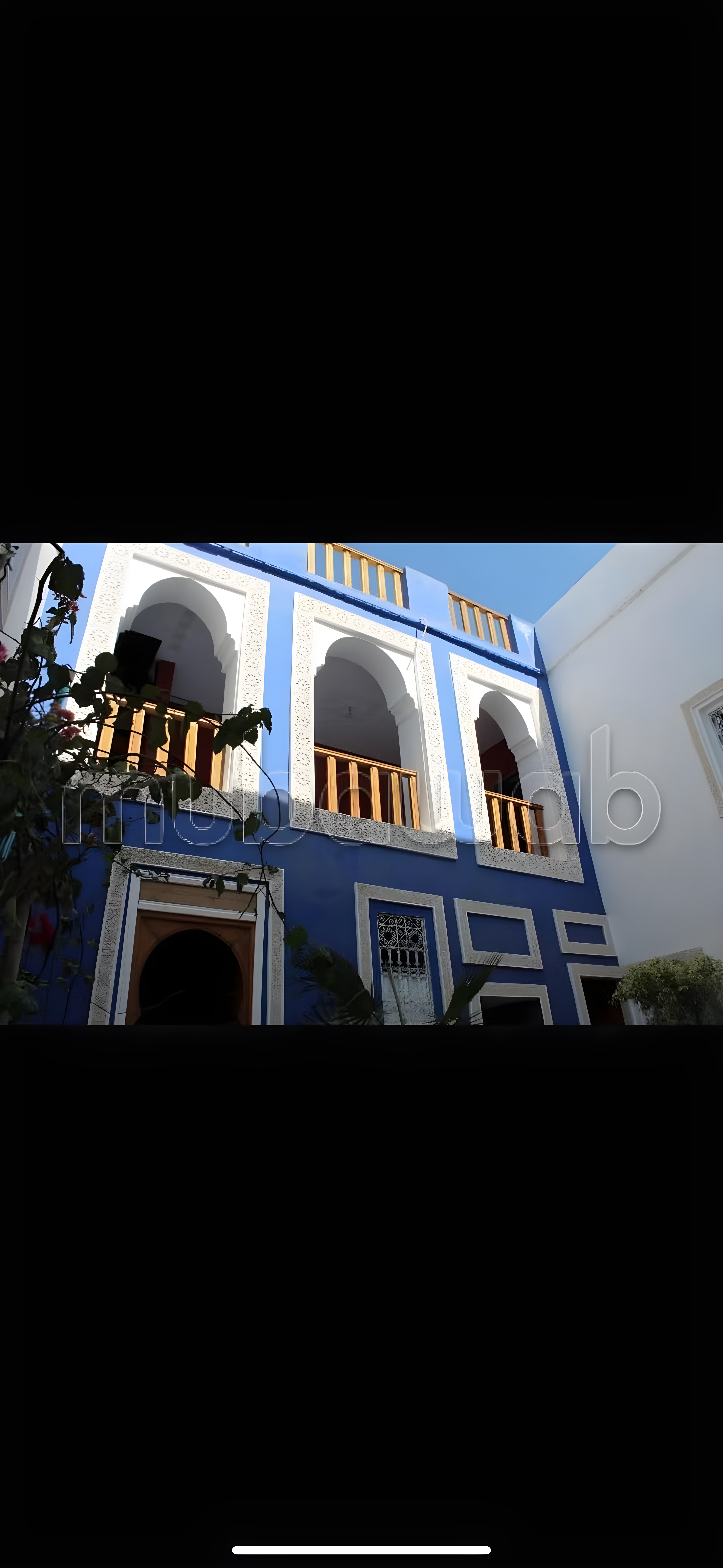 Facade of a Moroccan guesthouse with blue walls, arches, and wooden balcony in Bab Aylan.