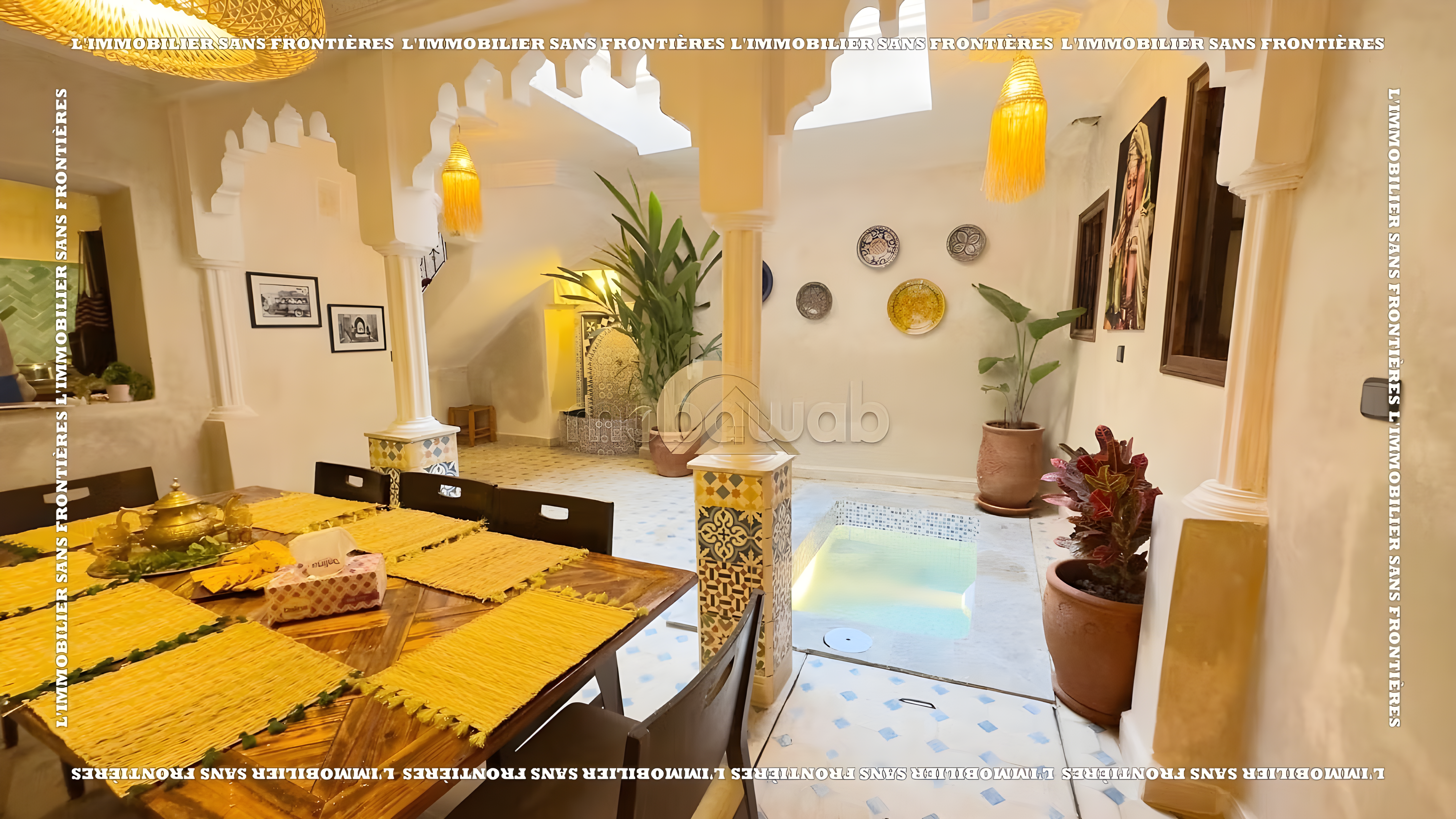 Moroccan courtyard with columns, plants, dining furniture, and lighting in Rmila riad.
