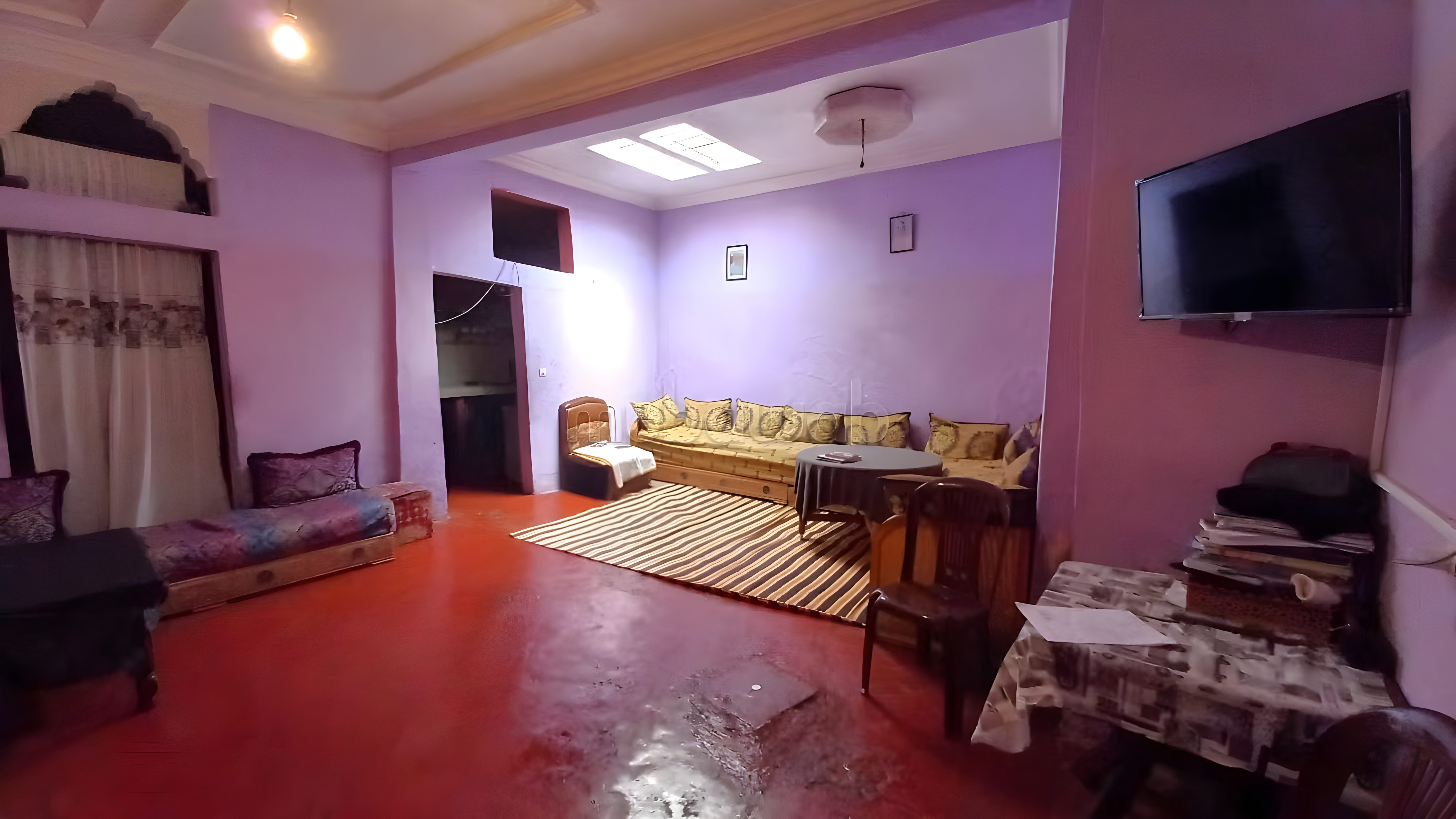 Salon with purple walls, red floors, wooden furniture, a TV, and skylight in Bab Lhmar guesthouse.