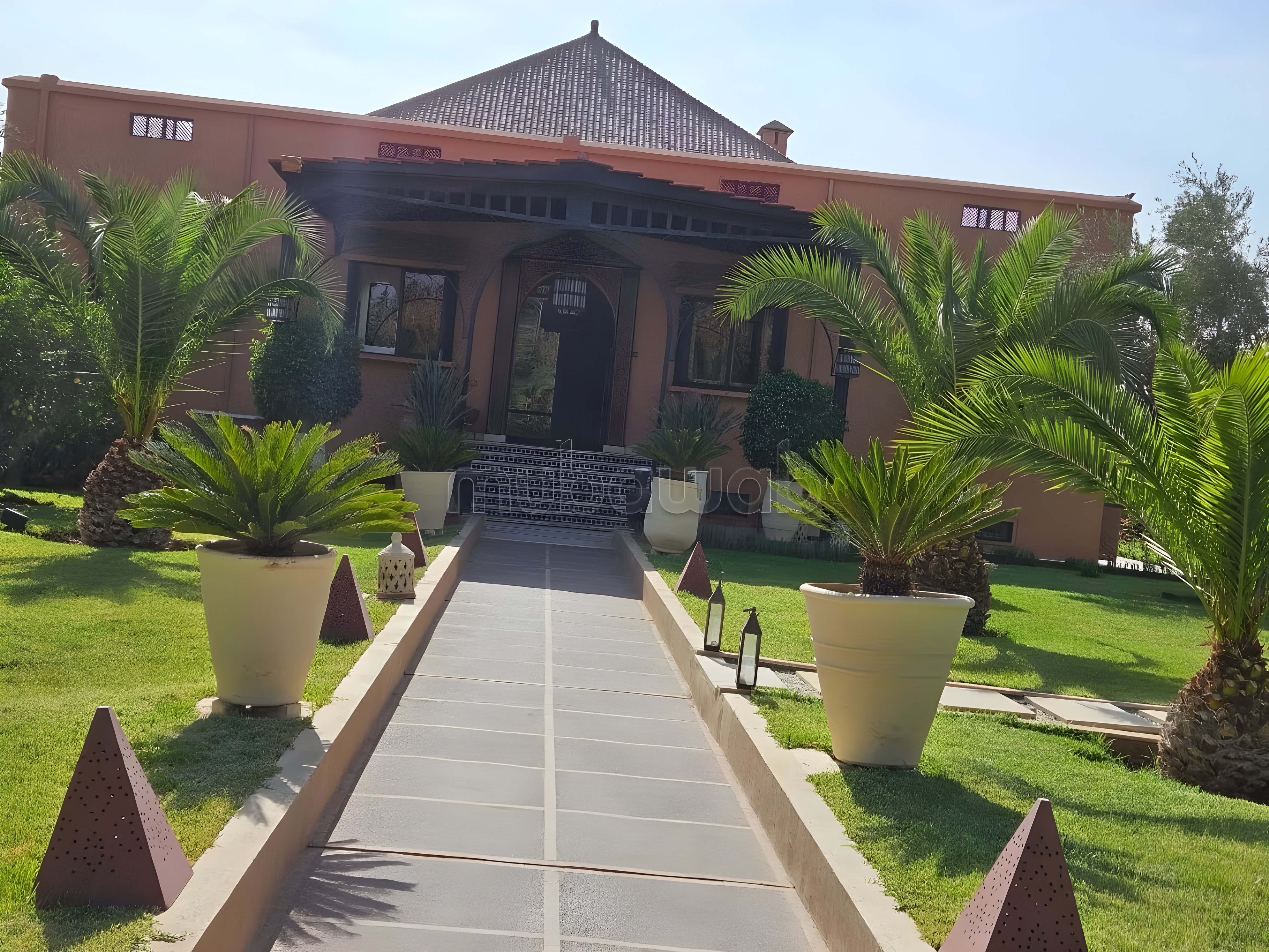 Facade of a Moroccan guesthouse on Route Amizmiz with potted plants lining the pathway.