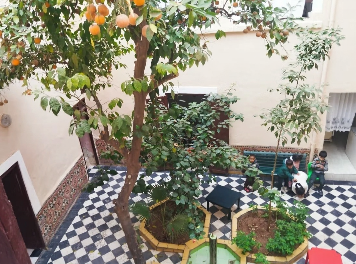 Courtyard with checkered tiles, fruit trees, seating, and doorways in Riad Zitoun.