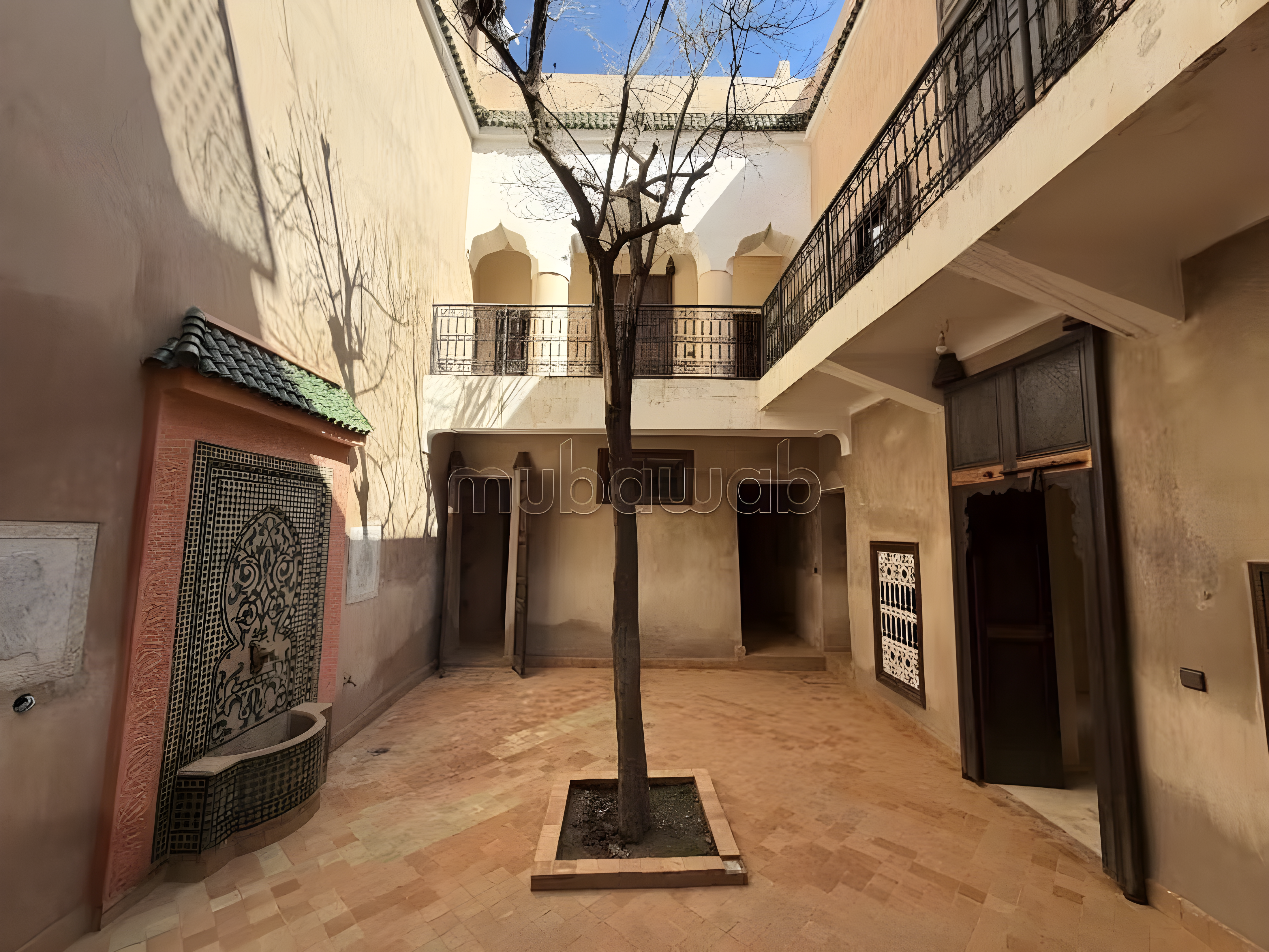 Courtyard with tiled flooring, central tree, and Moroccan architectural walls.
