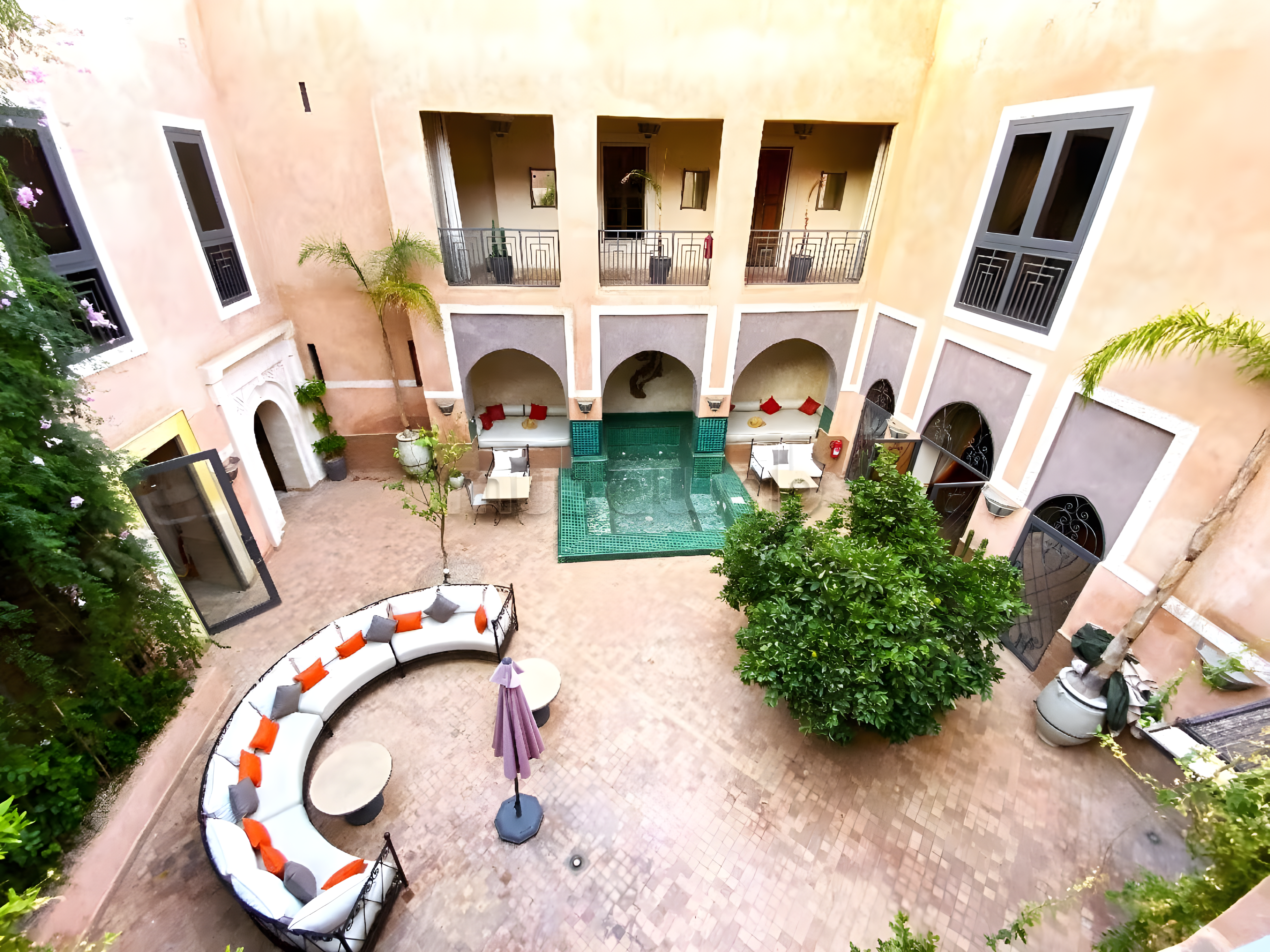 Courtyard of Moulay Lyazid guesthouse with arches, windows, seating, trees, and a central fountain.
