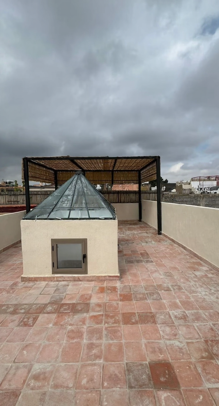Rooftop with terracotta flooring, pergola, and glass skylight in Moulay Lyazid guesthouse.