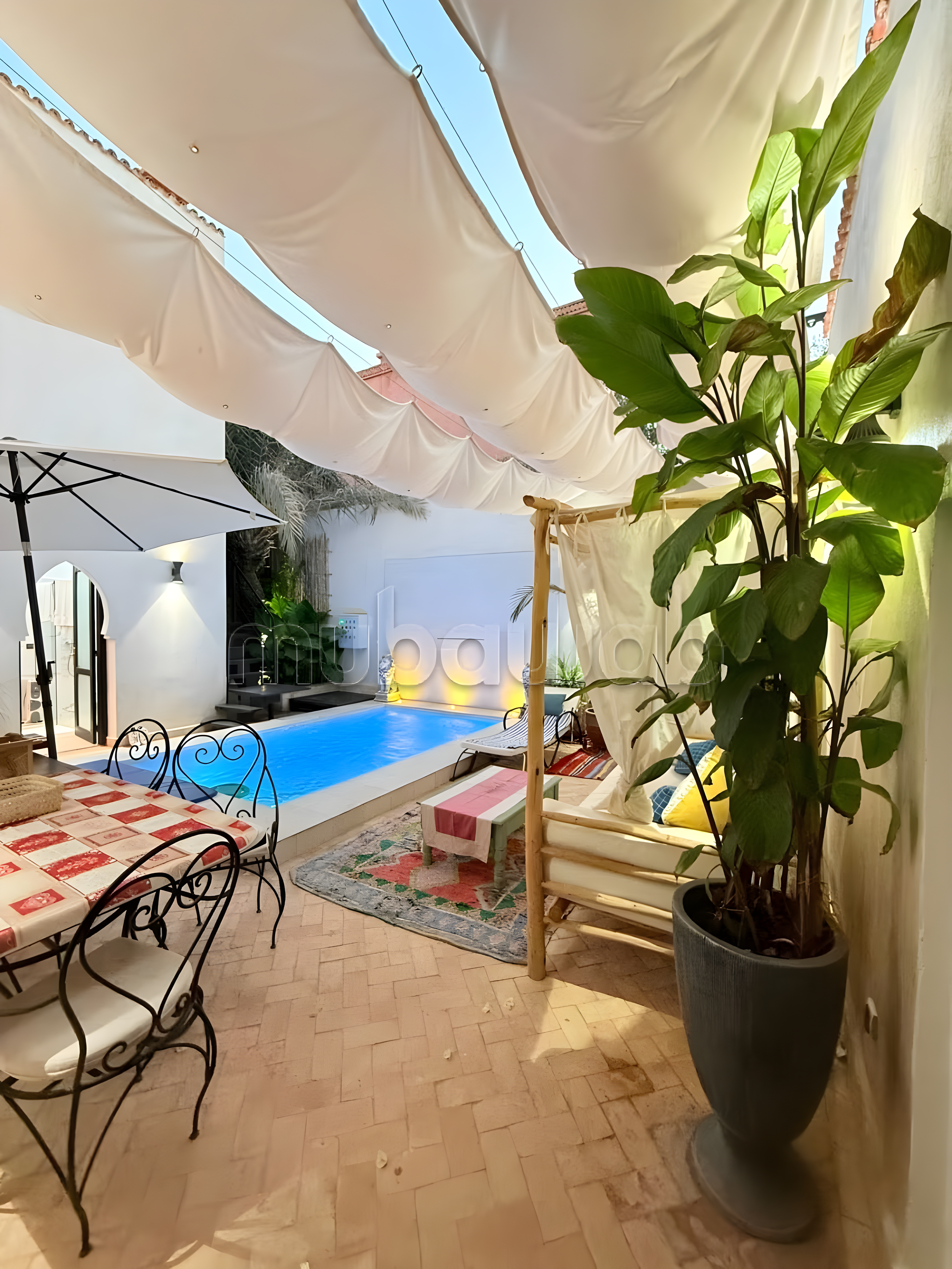 Courtyard of a guesthouse in Ennakhil with seating, dining table, pool, and shaded plants.