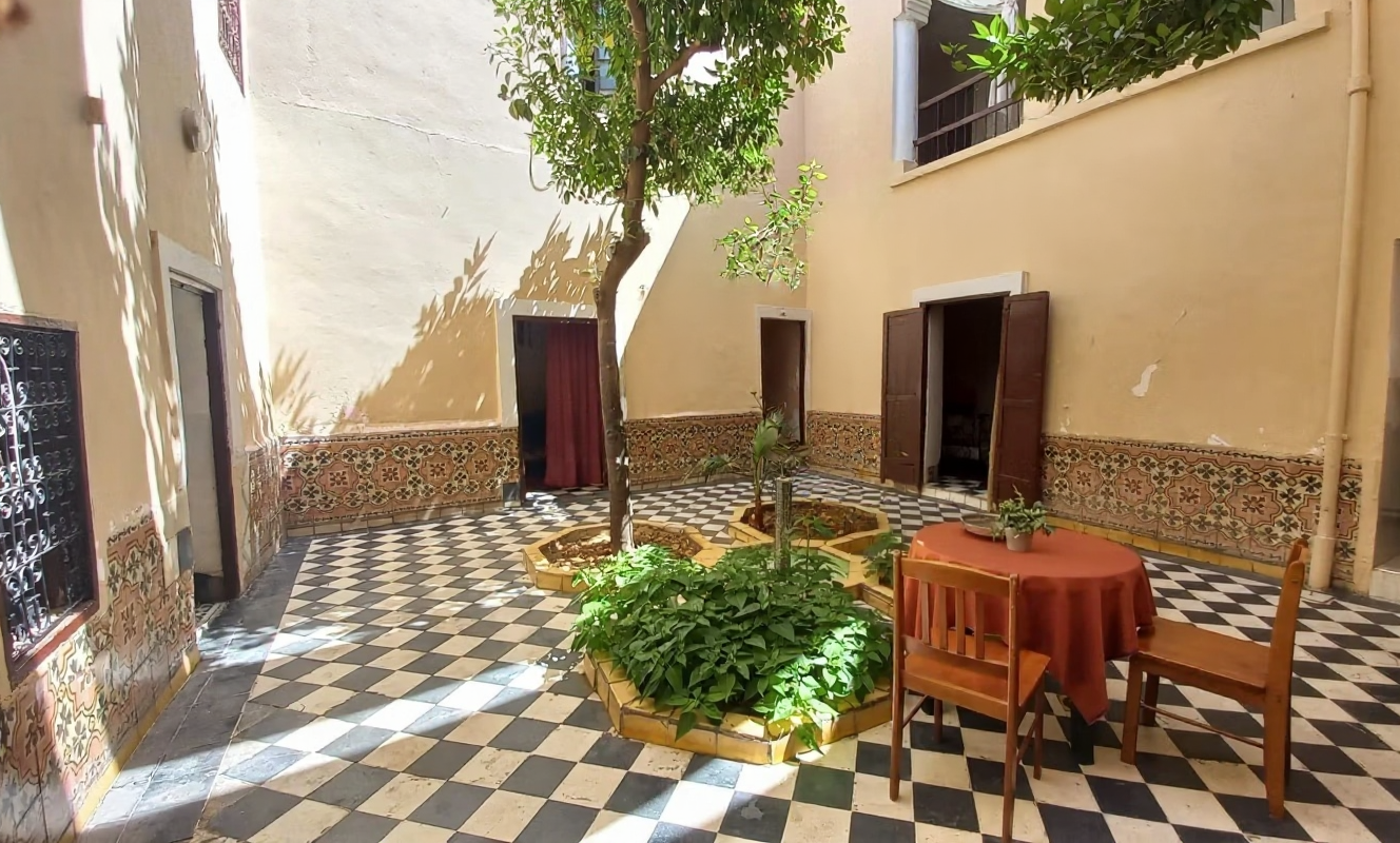 Courtyard with patterned tiles, plants, and a table with a red cloth in Riad Zitoun.