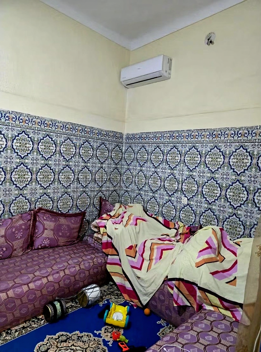 Cozy salon with patterned tile walls, corner sofa, and air conditioner in El Moukef guesthouse.