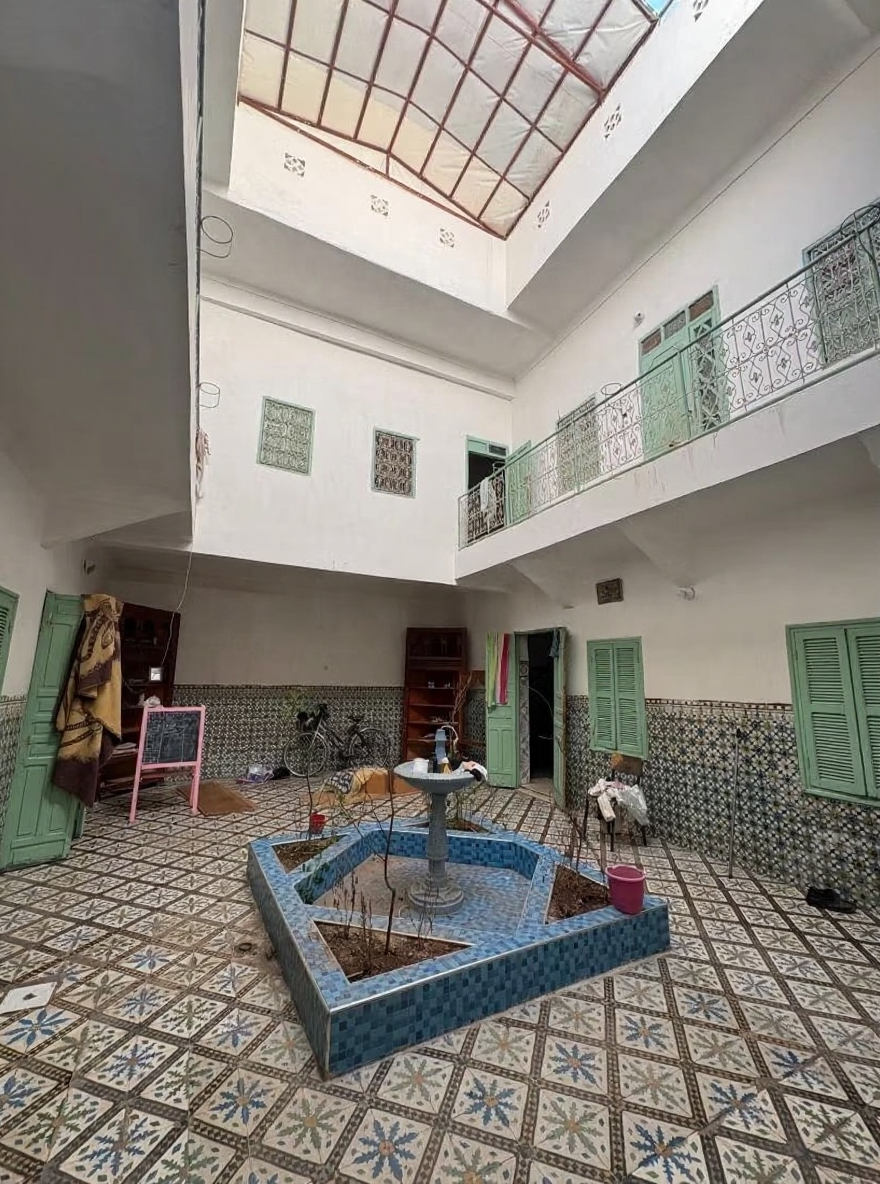 Guesthouse courtyard with tiled flooring, fountain, balconies, and green shutters in Sidi Ben Slimane El Jazouli.